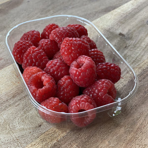 punnet of fresh raspberries on a wooden board
