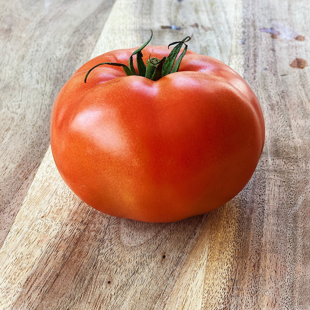 single beefsteak tomato on a wooden board