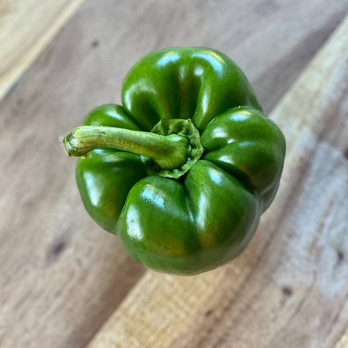 glossy green pepper on a wooden board