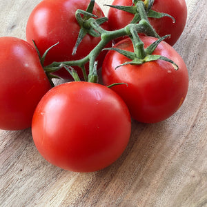 group of 5 red tomatoes on a vine on a wooden board
