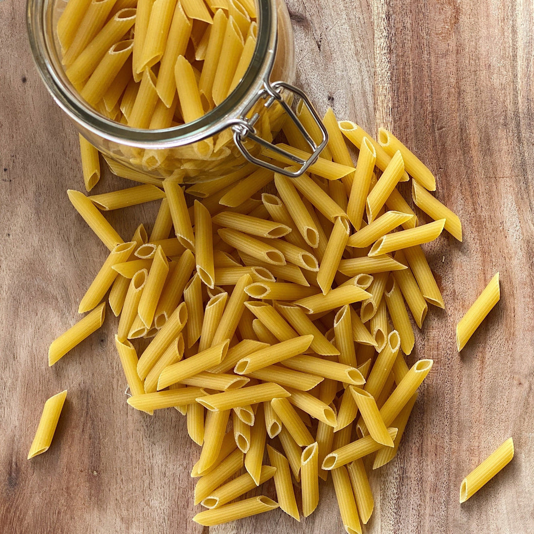 penne pasta on a wooden board with a jar of penne above