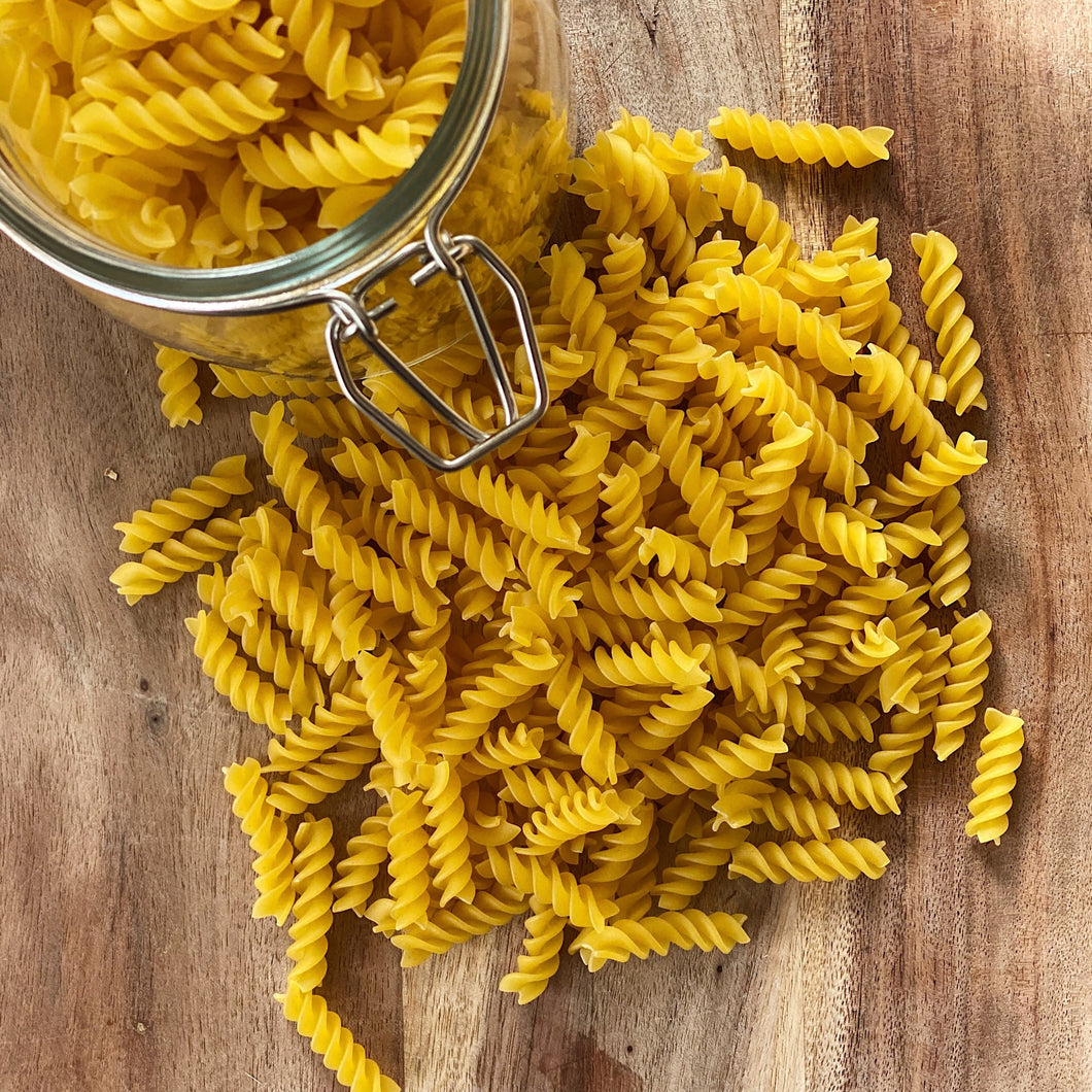 spiral fusili past on a wooden board with a jar of pasta next to it