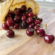 Load image into Gallery viewer, cherries spilling out of a paper bag onto a wooden board

