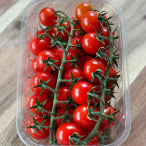 punnet of red cherry vine tomatoes on a wooden board