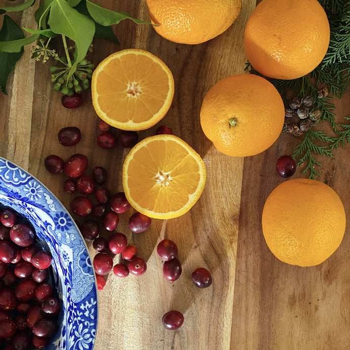 Fresh Oranges, one cut open on a wooden board with cranberries in a bowl with foliage