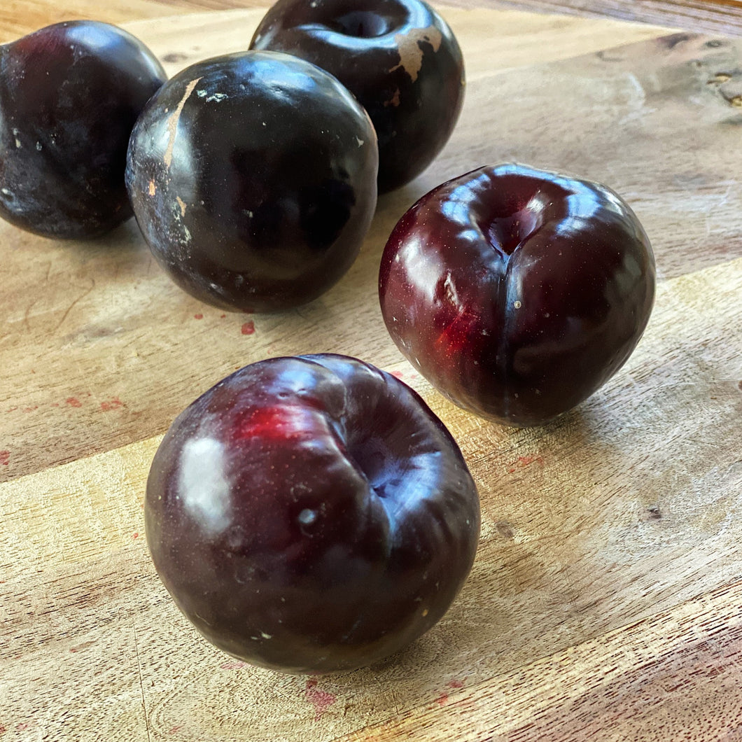 5 glossy purple plums on a wooden board