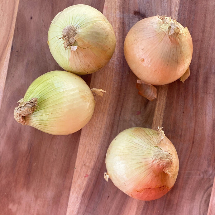 4 raw white onions on a wooden board