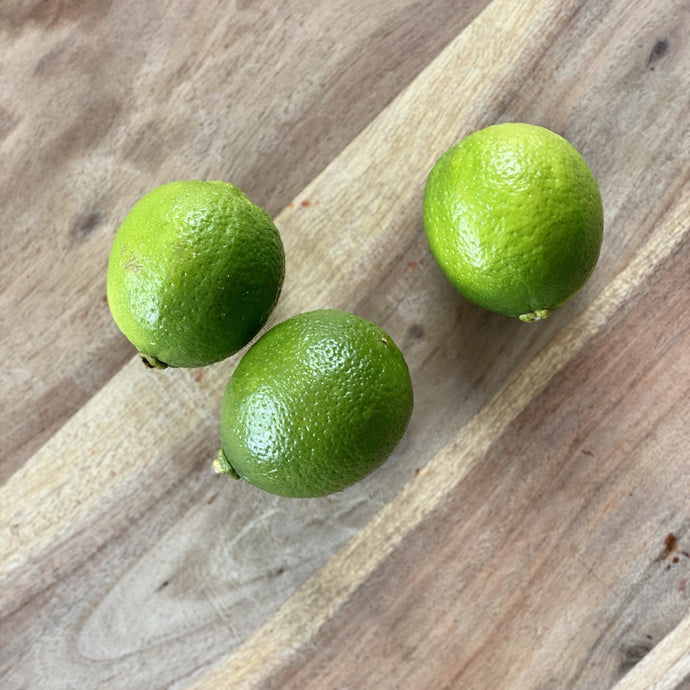 3 fresh green limes on a wooden board