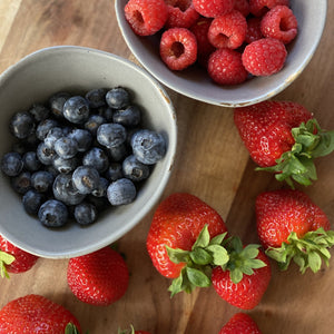 blueberries and rasberries in bowls and loose strawberries on a wooden board